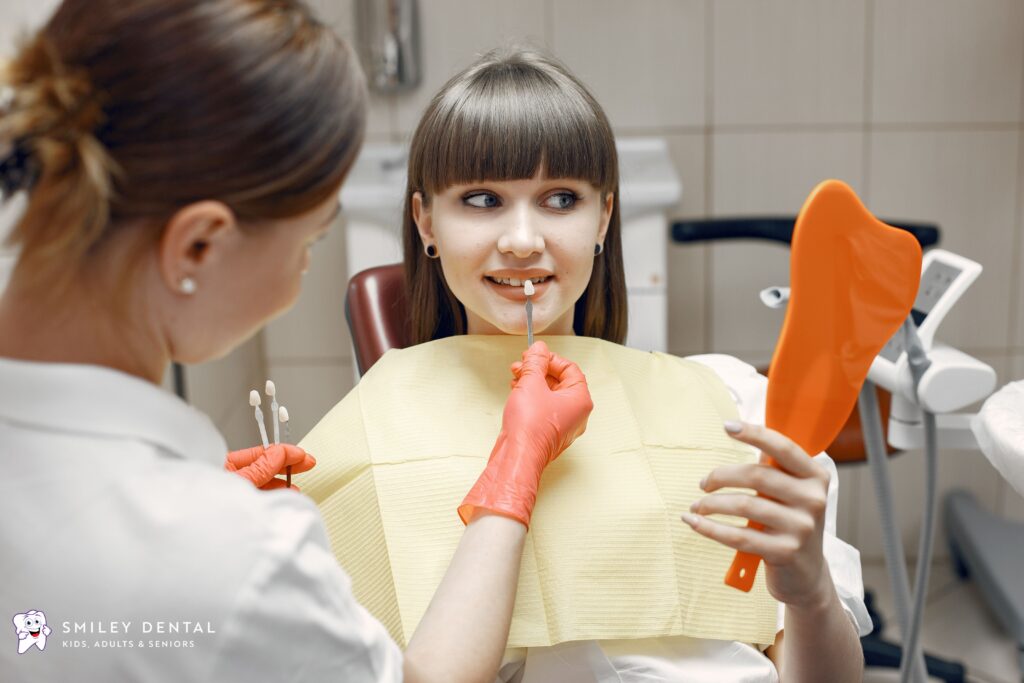 Dentist checking tooth shade with patient holding a mirror during a chipped front tooth consultation
