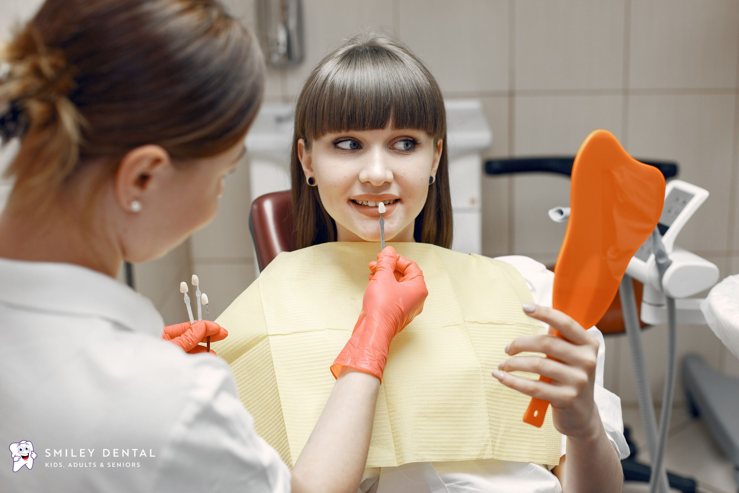 Dentist checking tooth shade with patient holding a mirror during a chipped front tooth consultation