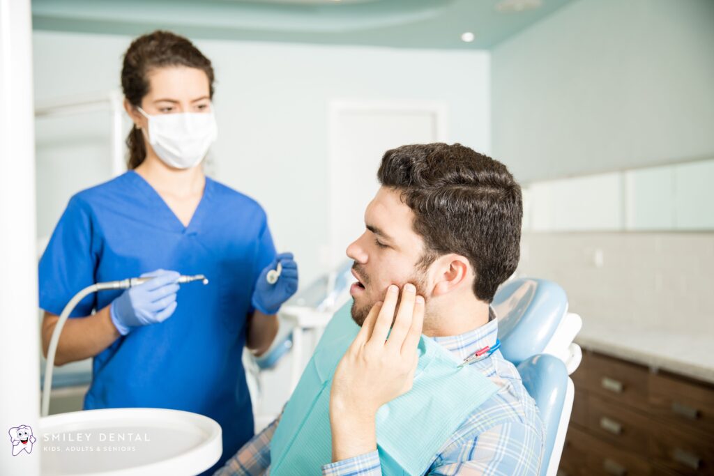 Man holding jaw in pain during emergency dental exam for possible root canal or tooth extraction in Roslindale