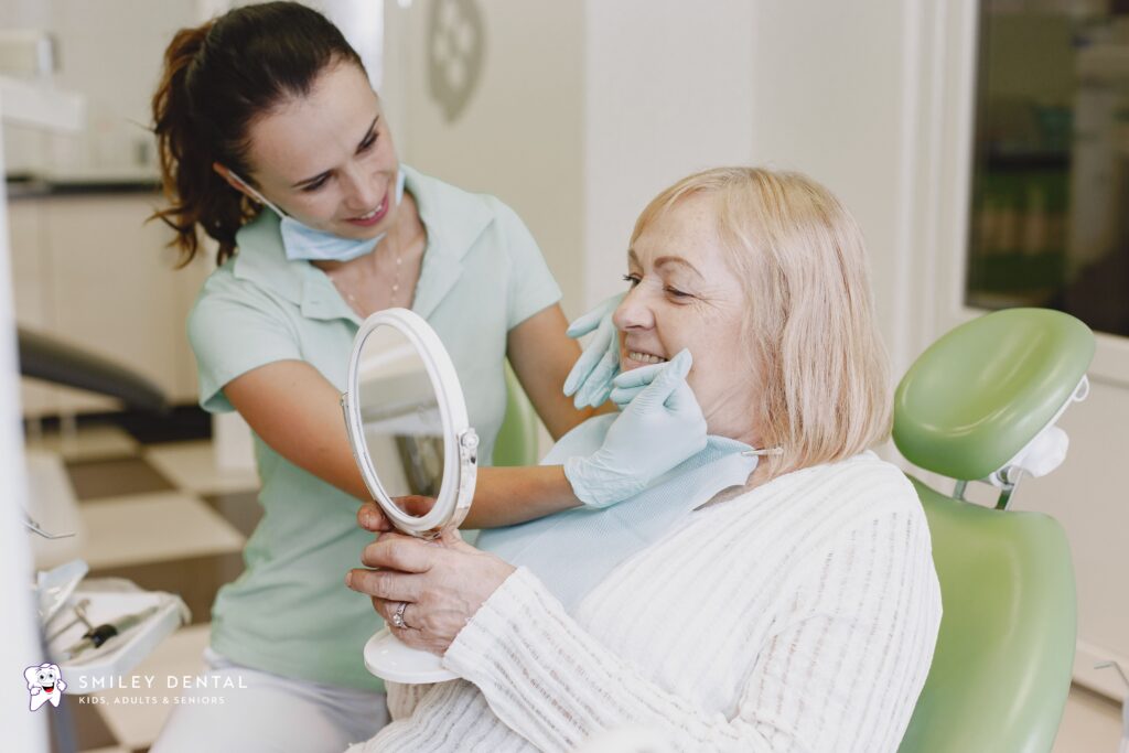 Dental assistant showing an elderly female patient her restored smile in a mirror at Smiley Dental Boston