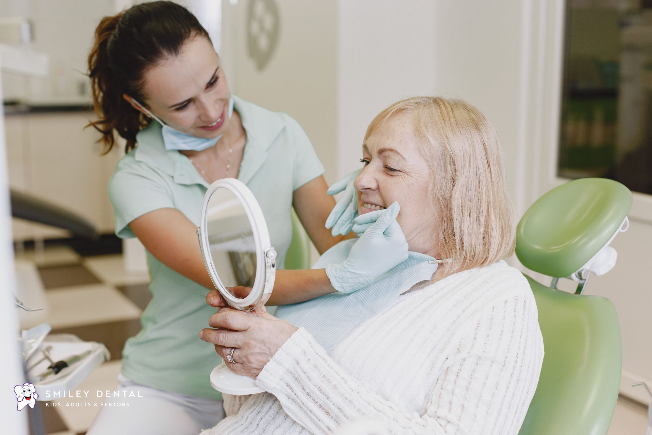 Dental assistant showing an elderly female patient her restored smile in a mirror at Smiley Dental Boston