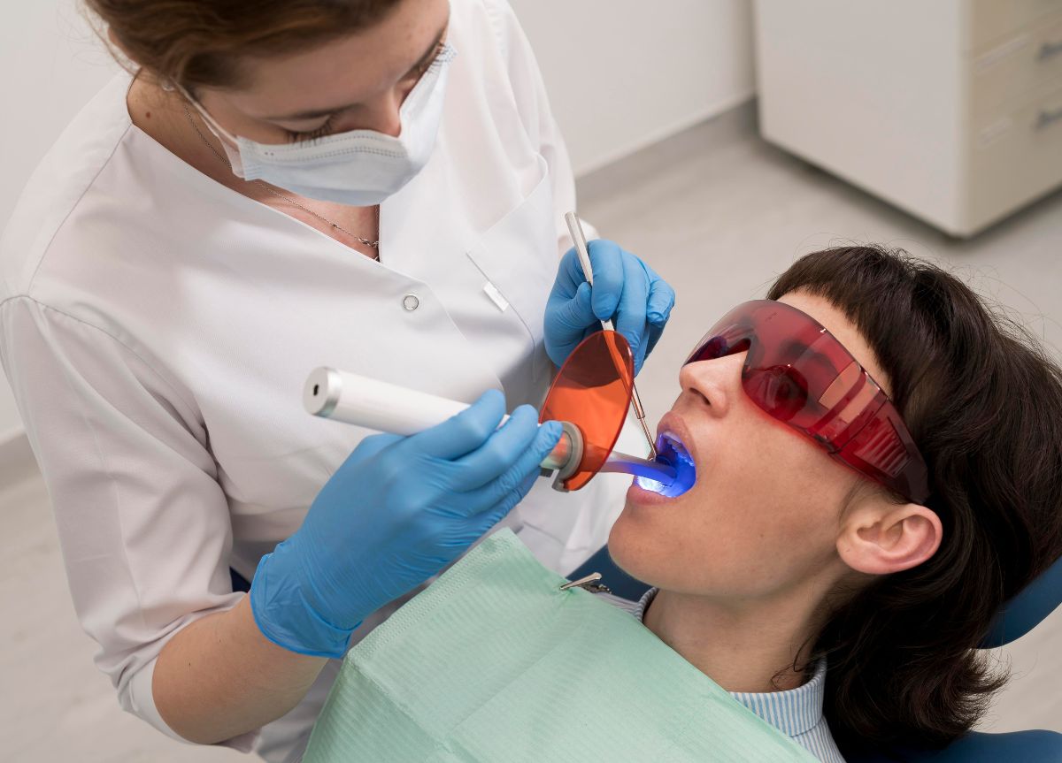 Dentist performing professional teeth whitening treatment with UV light on patient in Boston dental office
