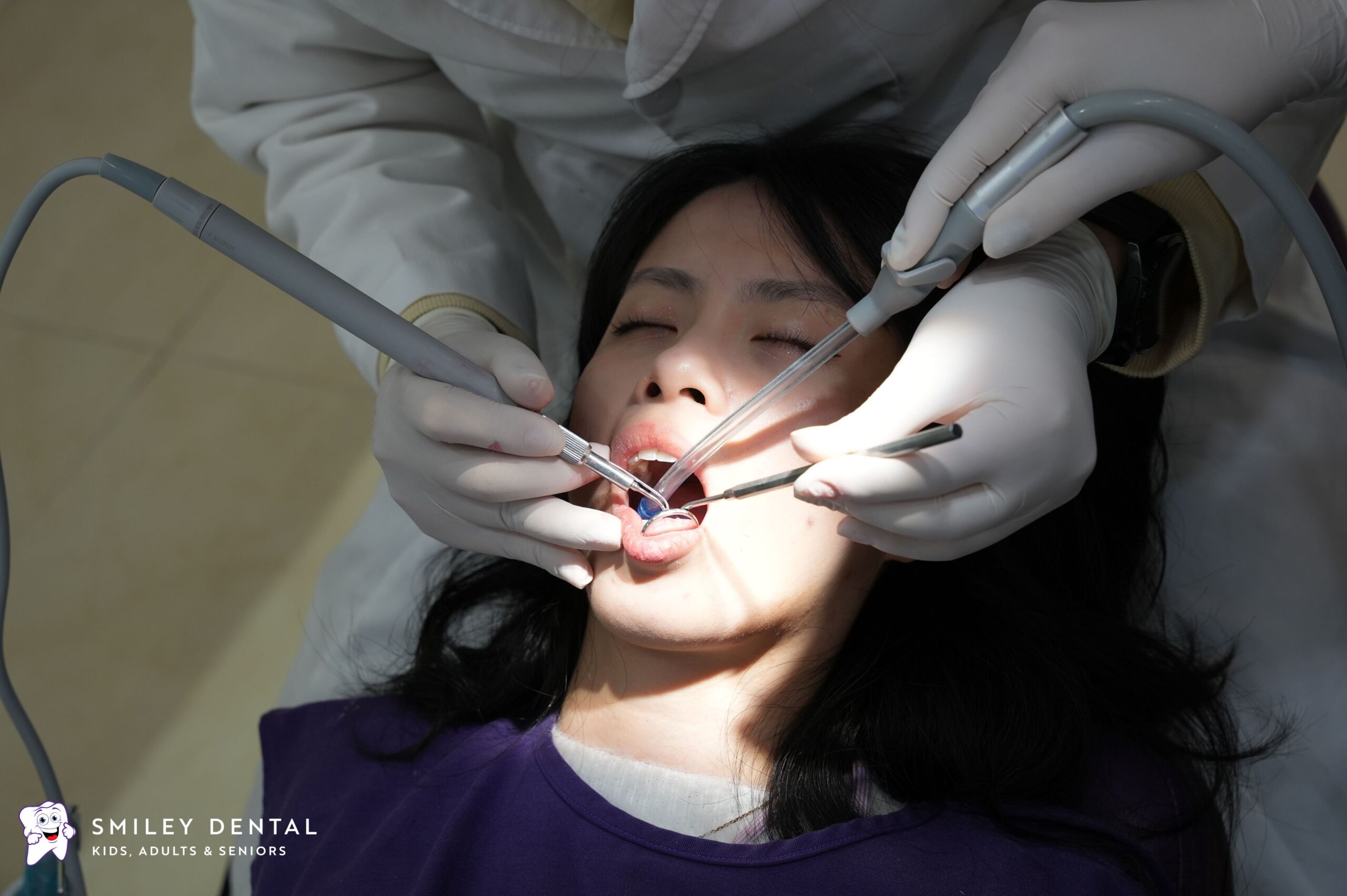 Dentist performing dental treatment on a patient using suction and dental instruments