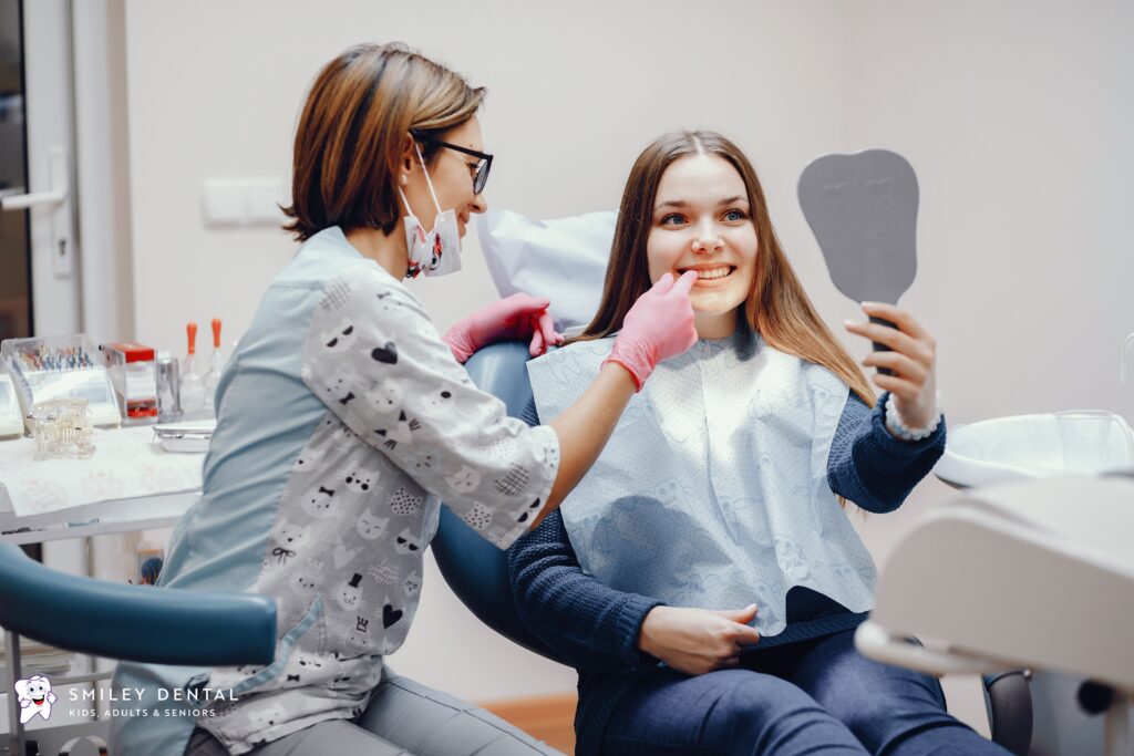 Smiling patient looking at her whiter teeth in a mirror after a professional whitening treatment