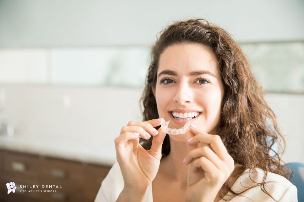Smiling woman holding a clear Invisalign aligner, illustrating Invisalign cost in Boston