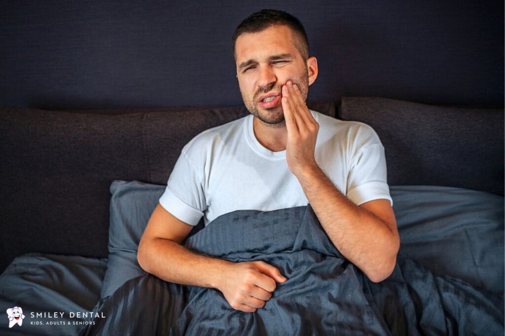 Man holding jaw in pain from toothache at night while sitting in bed